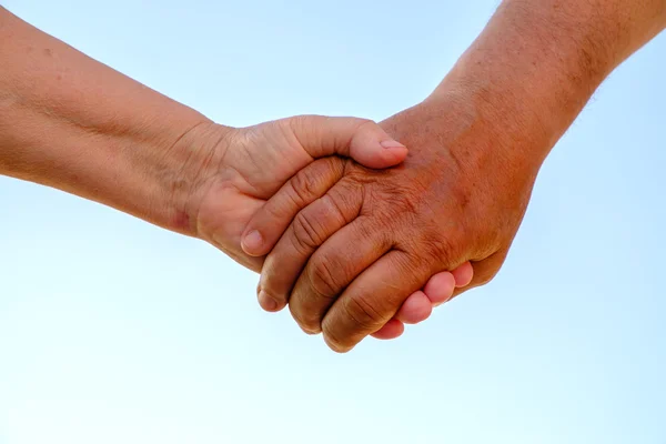 Elderly couple holding hands on the background of blue sky — Stock Photo, Image