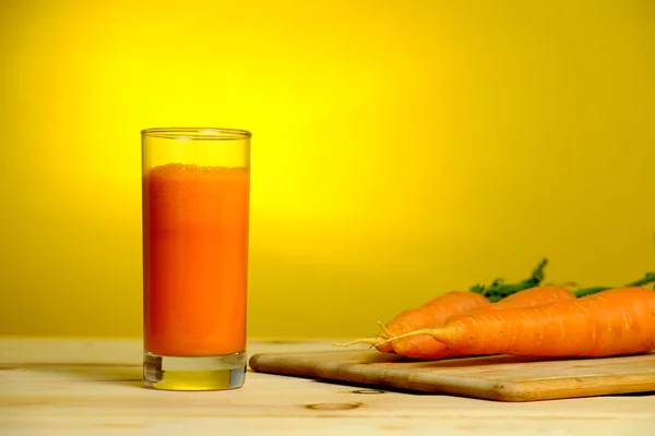 Fresh carrot juice in glass on yellow background — Stock Photo, Image
