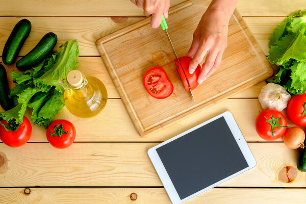 Woman cutting tomato and using tablet in her kitchen