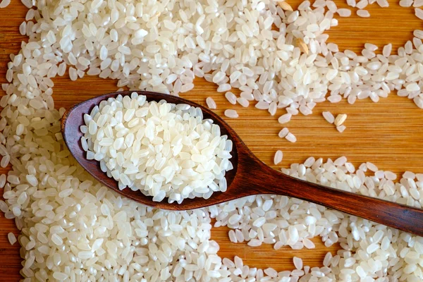 Grano de arroz en cuchara de madera oscura sobre tabla de madera —  Fotos de Stock