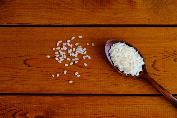 Grano de arroz en cuchara de madera oscura sobre tabla de madera, vista superior —  Fotos de Stock