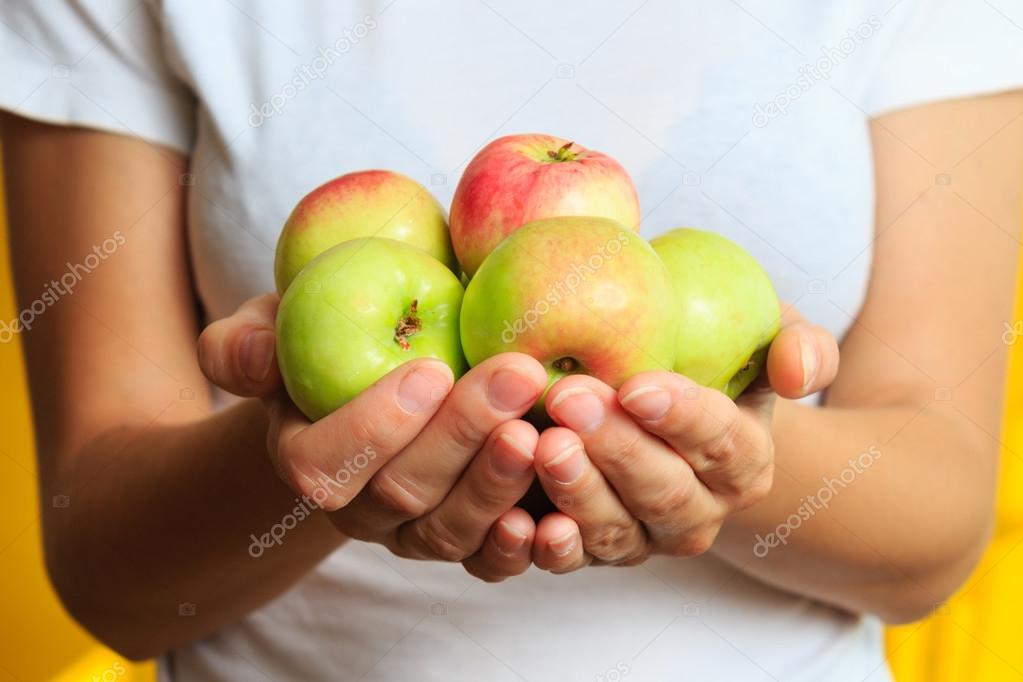Woman in white t-shirt is holding fresh sweet green apple in his hands