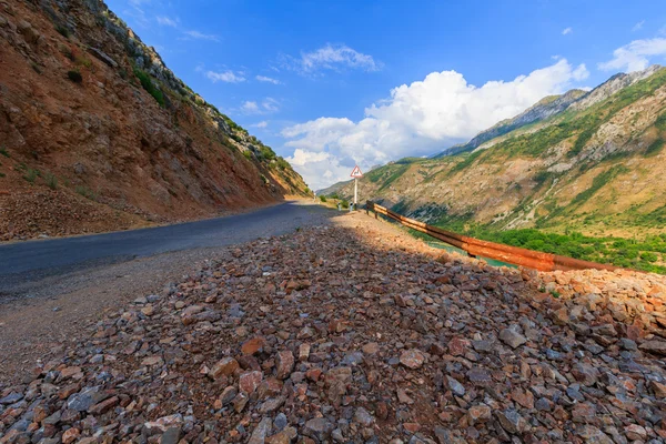 Jalan yang rusak di pegunungan dan tanda tikungan yang berbahaya . — Stok Foto