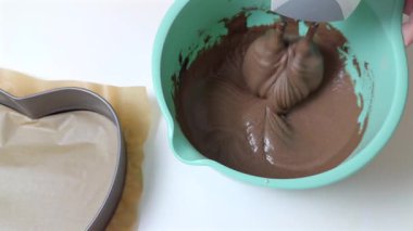 Çikolatalı kek hamuru bir kasede elektrikli el mikseriyle karıştırılıyor. Sahnede düzgün bir karışım, döner çırpıcı ve ev yapımı kek pişirmeden önce etkin bir hazırlık adımı gösteriliyor..