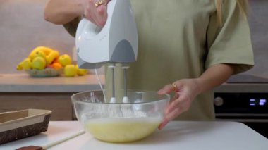 Mutfak tezgahında cam bir kasede yumurtaları elektrikli el mikseriyle karıştıran bir kadının yakın çekimi. Ev yemeği pişirme, yemek hazırlama, pişirme ya da tatlı malzemeleri..