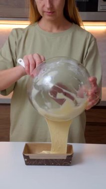 Bir kadının cam kaseden mutfak tezgahındaki dikdörtgen bir tavaya pürüzsüz kek hamuru dökerkenki yakın çekimi. Ev yapımı pişirme, tatlı hazırlama ve modern mutfak içinde ev yapımı gıda konsepti..