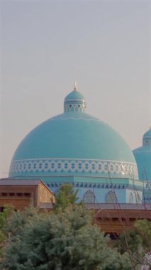 Ağaçların üzerinden gökyüzüne yükselen bir caminin turkuaz kubbesi. İslami mimari, dini yapı dış ve kültürel dönüm noktası kavramı.