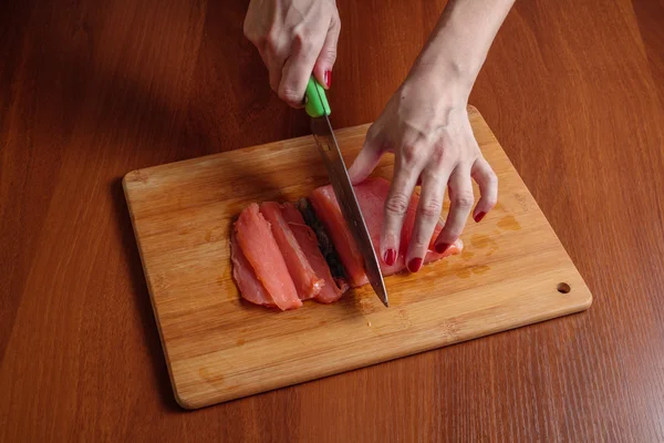 Manos de mujer rebanando pescado con un cuchillo en una mesa de madera — Foto de Stock