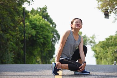Ayak bileği incinen bir koşucu bileğini burktu ve acı verici bir ifadeyle bileğini burktu..