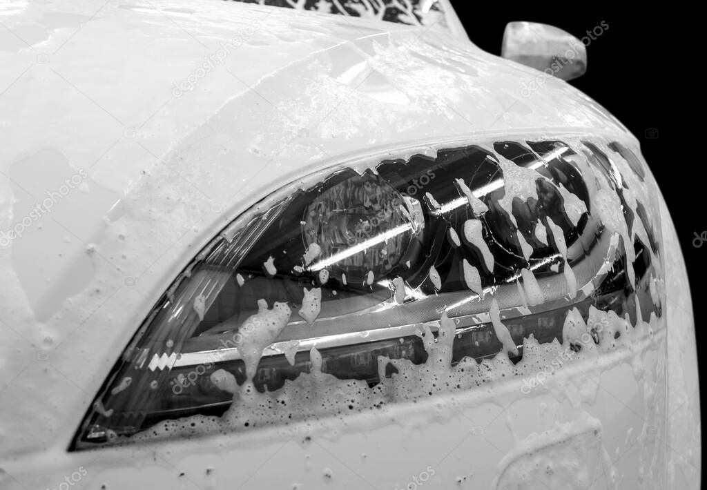 Modern car wash with soap. Auto headlamp covered by foam.