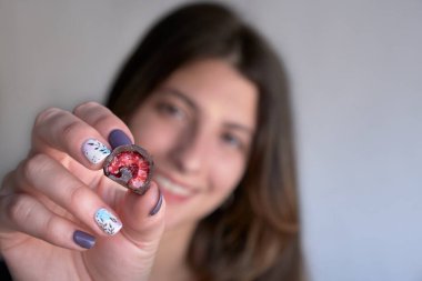 Kadının eli taze kırmızı ve parlak ahududu seçiyor ve alıyor. Ev yapımı siyah beyaz çikolataya batırılmış.