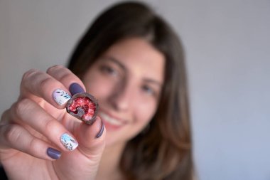 Kadının eli taze kırmızı ve parlak ahududu seçiyor ve alıyor. Ev yapımı siyah beyaz çikolataya batırılmış.