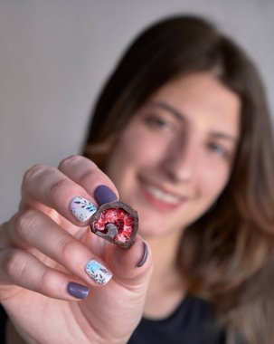 Kadının eli taze kırmızı ve parlak ahududu seçiyor ve alıyor. Ev yapımı siyah beyaz çikolataya batırılmış.