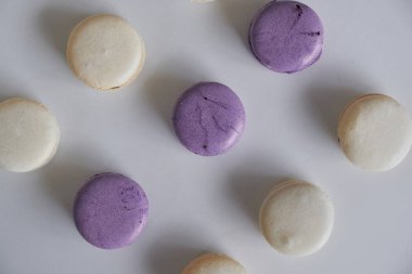 Beyaz ve siyah çikolata soslu beyaz bir masada mor ve beyaz badem ve badem kurabiyesi ve krem şanti..