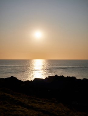 Sahil şeridinin uzun pozlama manzarası: sudaki günbatımının renkleri kayalar ve gökyüzü
