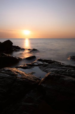 Sahil şeridinin uzun pozlama manzarası: sudaki günbatımının renkleri kayalar ve gökyüzü