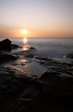 Sahil şeridinin uzun pozlama manzarası: sudaki günbatımının renkleri kayalar ve gökyüzü