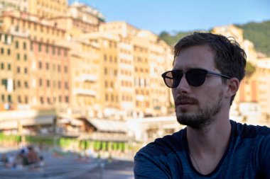 Camogli, Cenova, İtalya sahillerinde renkli evlerin arkasında güneş gözlüğü takan genç bir modelin portresi.