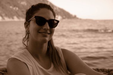 Sahilde güneş gözlüğü takan genç bir model. İtalya, Liguria, Camogli plajı. Arka planda renkli evler var.