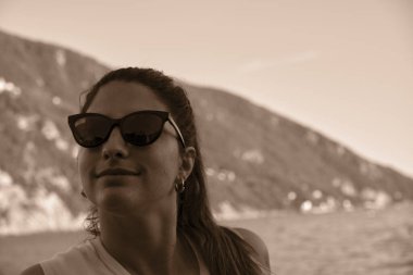 Sahilde güneş gözlüğü takan genç bir model. İtalya, Liguria, Camogli plajı. Arka planda renkli evler var.