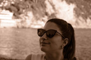 Sahilde güneş gözlüğü takan genç bir model. İtalya, Liguria, Camogli plajı. Arka planda renkli evler var.