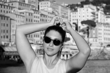 Sahilde güneş gözlüğü takan genç bir model. İtalya, Liguria, Camogli plajı. Arka planda renkli evler var.