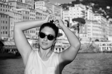 Sahilde güneş gözlüğü takan genç bir model. İtalya, Liguria, Camogli plajı. Arka planda renkli evler var.
