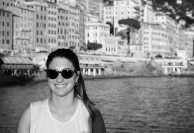 Sahilde güneş gözlüğü takan genç bir model. İtalya, Liguria, Camogli plajı. Arka planda renkli evler var.