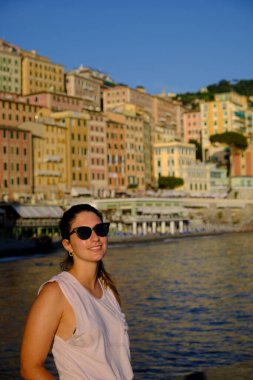 Sahilde güneş gözlüğü takan genç bir model. İtalya, Liguria, Camogli plajı. Arka planda renkli evler var.