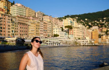 Sahilde güneş gözlüğü takan genç bir model. İtalya, Liguria, Camogli plajı. Arka planda renkli evler var.