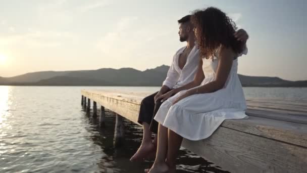一对异性恋的混血儿坐在湖畔的一个码头上 看着夕阳西下的夕阳西下的夕阳西下 — 图库视频影像