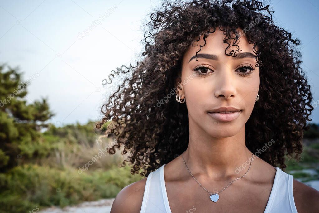 Femininity and beauty in nature: close up portrait of beautiful black Hispanic young woman with curly dark long hair looking confident at the camera - Make-up female artist with perfect mouth and eyes