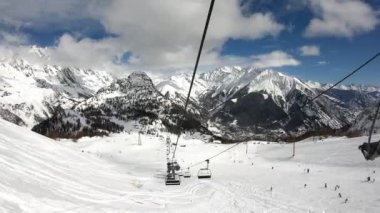 Courmayeur 'daki Mont Blanc kayak merkezinin kablosundan alınan 4K UHD hiperlapesi, arka planda Alpler' in mavi gökyüzünde güneş tarafından aydınlatılan dağ sıraları karla dolu.