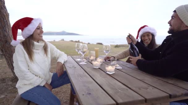 Drie Gemengde Race Vrienden Zitten Een Tafel Buiten Santa Hoeden — Stockvideo