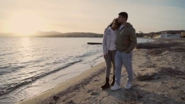 Gün batımında sahilde yürüyen genç heteroseksüel çok ırklı çiftin romantik sahnesi. Yakışıklı bir adam aşık kız arkadaşını kucaklıyor.