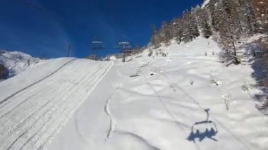 Kar kaplı Mont Blanc 'ın tepesindeki kayak yamaçlarına giden yarı boş bir teleferiğin HD hiperlapesi, güneşli güzel bir günde kar üzerinde oturan kayakçıların gölgesini düşürüyor.