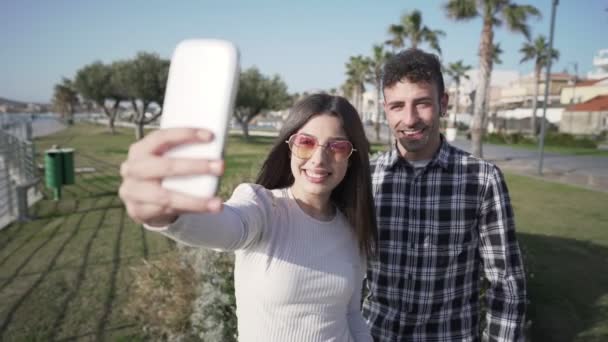 海のリゾートで休暇中の観光客の若い白人カップルは 遠くの友人とチャットするためにスマートフォンを使用しています 2人のブロガーは ソーシャルネットワーク上のスマートフォン共有の旅で自分自身を撮影します — ストック動画