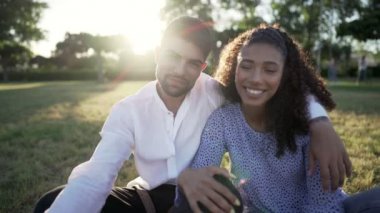 Gün batımında ya da gün doğumunda şehir parkında güneş ışığı efektiyle video görüşmesi yapan çok ırklı genç çiftin POV görüntüsü. Afrikalı kız ve beyaz adam konuşuyor, şaka yapıyor, öpüşüyor ve el sallıyor.