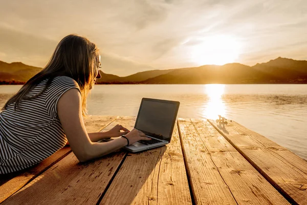 Yaratıcılığının tadını çıkaran genç bir kadın gün batımında bir iskelede kitap yazıyor. Modern zamanlarda her yerde çalışmak için yeni bir iş fırsatı. Laptop ve kablosuz internet bağlantısı teknolojisi kullanarak. Kız çalışıyor.