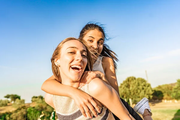 Yeşil bir doğa parkında eğlenen iki kız kameraya bakıp gülüyor ve şakalaşıyor. Sarışın kız arkadaşının arkasına atlayan genç esmer kadın ona sürpriz yapıyor. Mutlu öğrenciler