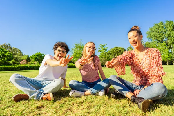 Três Jovens Estudantes Melhores Amigos Sentados Grama Parque Cidade Mostrando — Fotografia de Stock