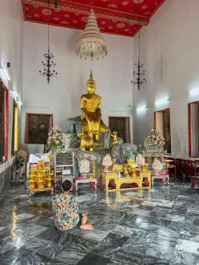 Bangkok, Tayland - 22 Ekim 2025: Bangkok 'ta kutsal bir tapınak salonunda elleri bağlı genç bir çocuk yerde oturuyor..