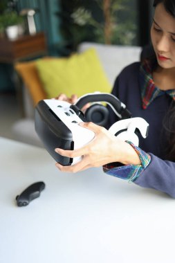 Evdeki oturma odasında sanal gerçeklik gözlüğü takan Asyalı genç bir kadın.