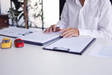 Araba kredisi, kira kontratı, araç ruhsatı ya da sigorta poliçesi için sözleşme imzalayan bir adam. Satış Sözleşmesi, Finansman Anlaşması, Sigorta Politikası, Araç Kaydı.