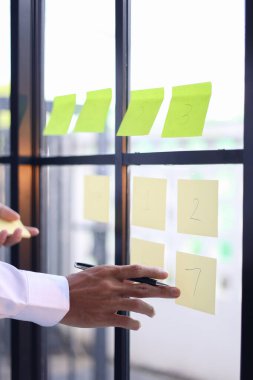 İş adamı düşünceleri düzenlemek, proje yönetimi ve beyin fırtınası için görevler planlamak için aynaya yapışkan notlar koyar.
