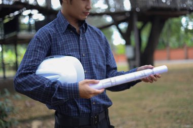 İnşaat mühendisi ya da mimar inşaat alanlarını ya da tasarım projelerini denetler, güvenlik kaskı ve planları ya da inşaat planları bulundurur..