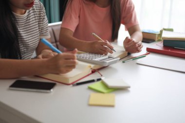 İki genç kız evde ders çalışırken not defterlerine yazıyorlar..