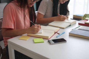 İki genç kız evde ders çalışırken not defterlerine yazıyorlar..