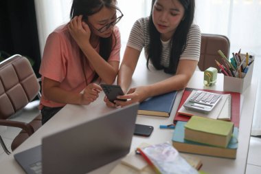 Evde ders çalışırken akıllı telefon kullanan iki kız öğrenci..