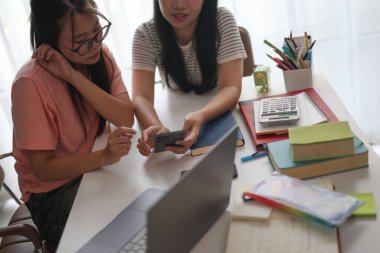 Evde ders çalışırken akıllı telefon kullanan iki kız öğrenci..